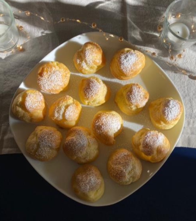 14 French cream puffs on a white plate with strays of sunlight making the plate shine!