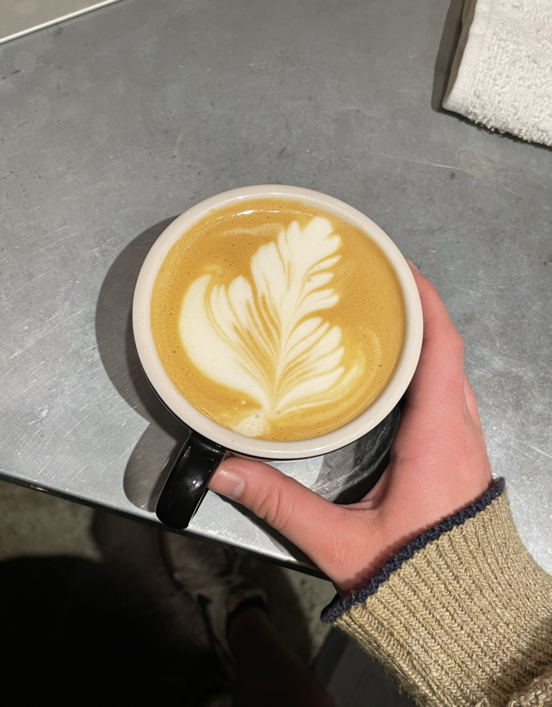 An image of a latte at slow train. The cup is light blue and has a feather drawn on the latte out of milk. 
