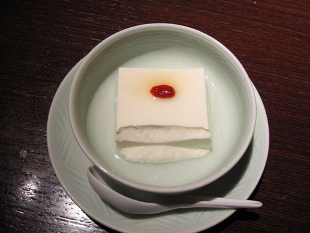 A bowl with a square cut of white Annin tofu, topped with a small red sweet apricot seed