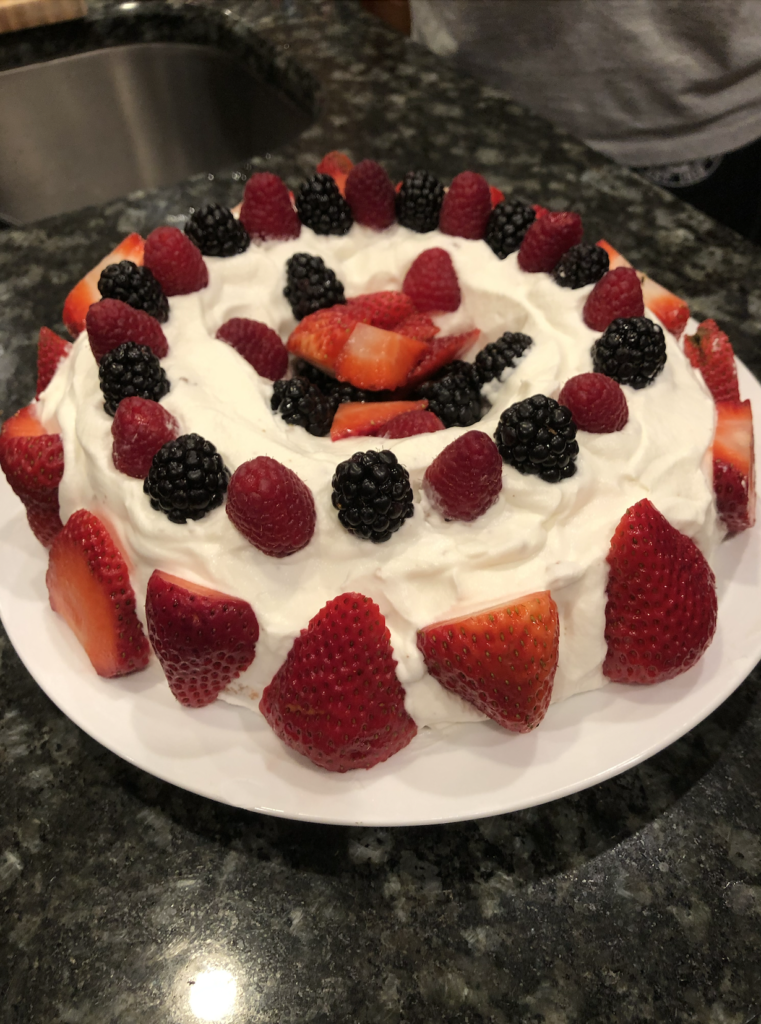 A bundt cake shaped chiffon cake, frosted with whipped cream and decorated with berries along the sides, top, and in the indented center.