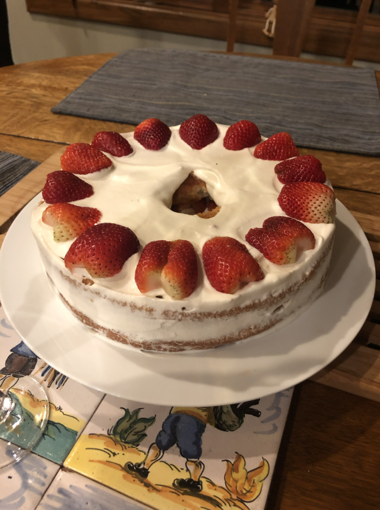 A chiffon cake sparsely coated on its sides but topped with halved strawberries on the top.