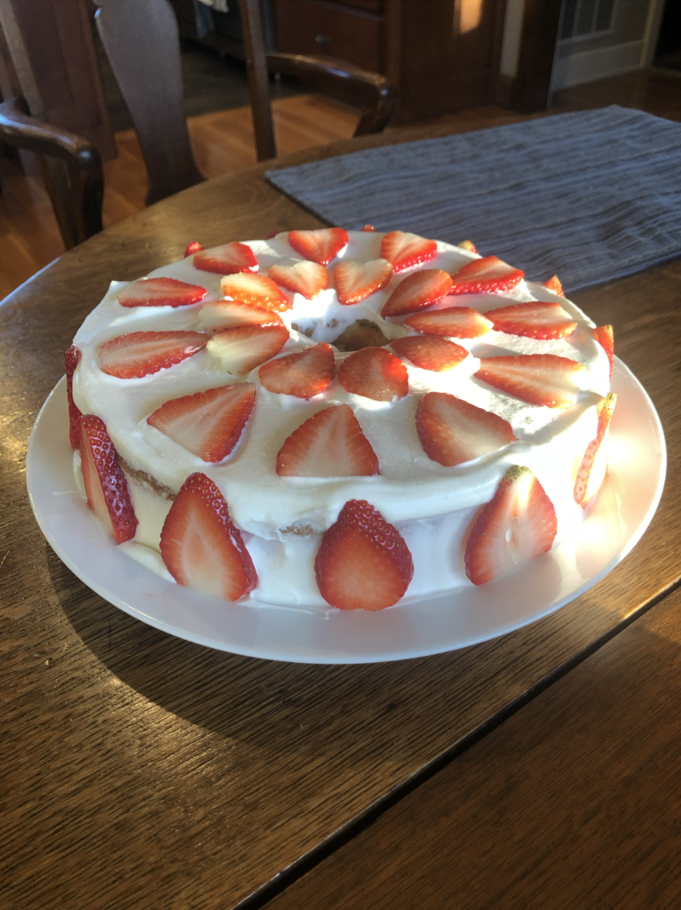 A chiffon cake in the sunlight, decorated with thinly sliced strawberries on the sides and forming two concentric circles on the top.