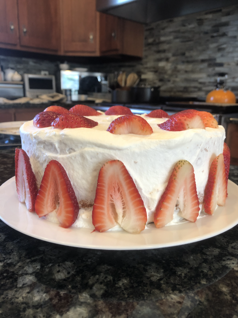 A tall chiffon cake from the side, the edge of the cake reaching beyond the height of the strawberries decorating its perimeter.