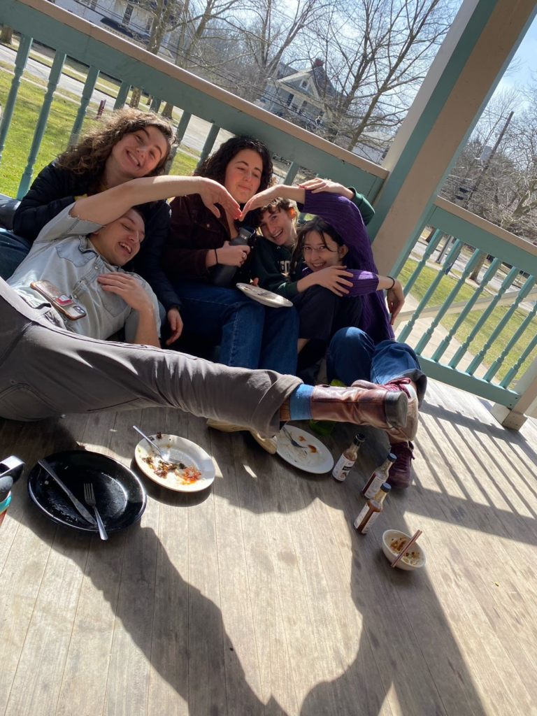 Photo of Oberlin students (left to right) Elijah, Bella, Lucy, Brooke, and Caterina forming a heart with their limbs during a lunch at Tank Co-op. Photo taken by Rhys Shepherd.